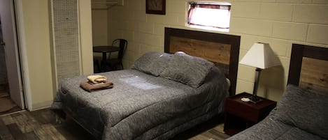 A bedroom with a single bed, a bedside table with a lamp, a chair, and a window with a curtain.