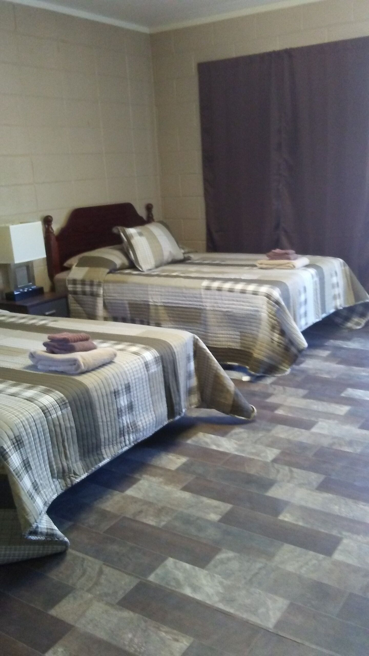 A hotel room with two beds, a large window with curtains, a flat-screen TV, and a small table with a lamp.