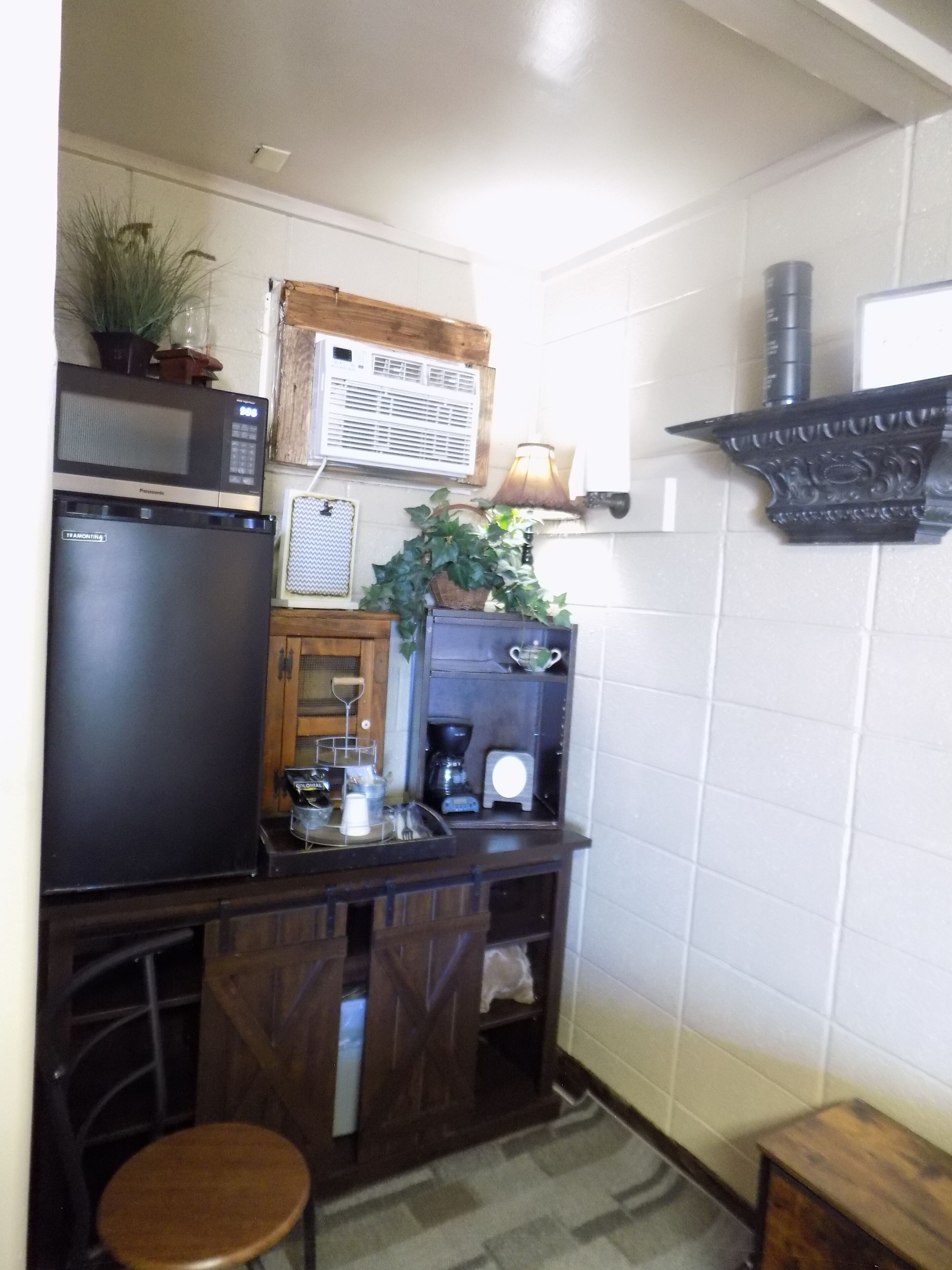Cocina compacta con refrigerador, microondas, cafetera y un pequeño comedor con un taburete.