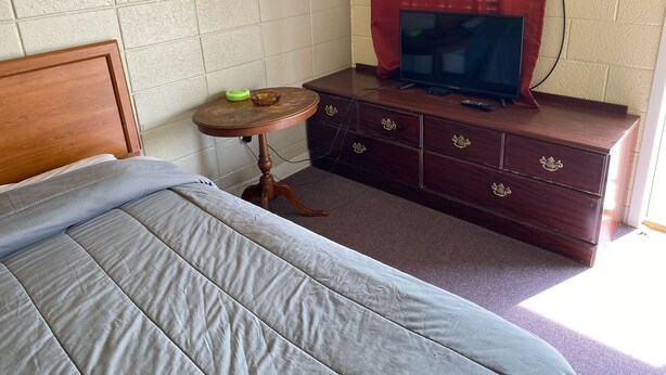 Un dormitorio con una cama, una mesita redonda con un cuenco, un aparador con cajones y un televisor encima.