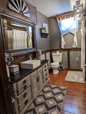 A bathroom with a wooden vanity, a large mirror, a toilet, and a shower curtain.