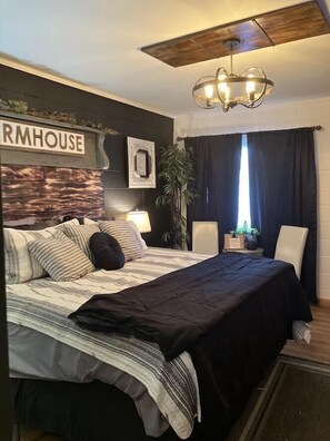 A bedroom with a bed, a nightstand, a lamp, a potted plant, and a sign that reads "RMHOUSE".