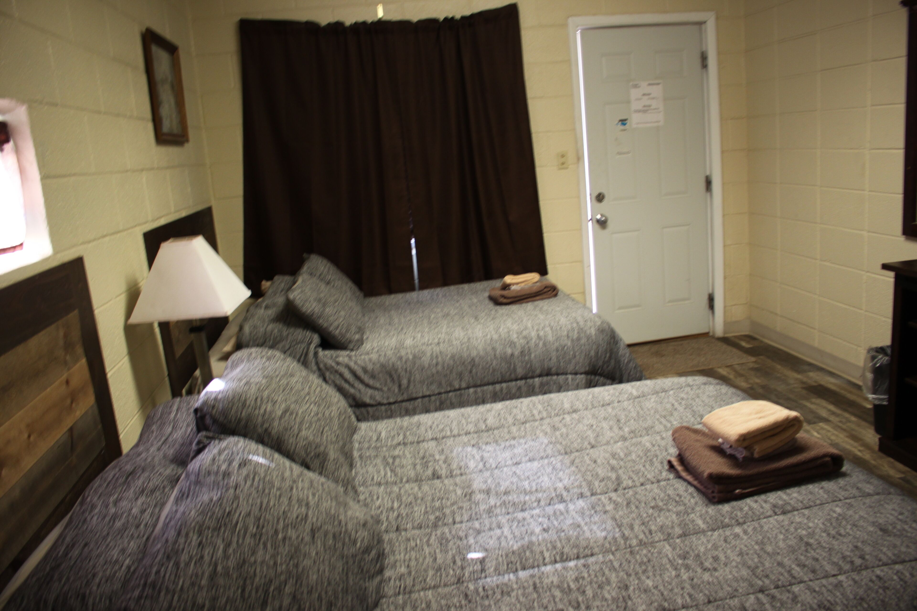 A hotel room with two beds, a lamp, a door, and a window.