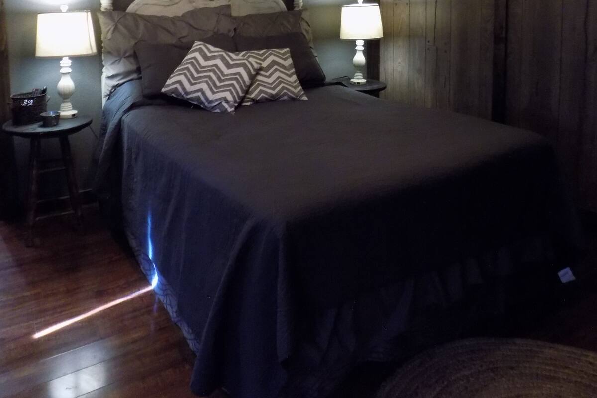 Quarto com cama, duas luminárias de cabeceira, um letreiro fixado na parede e cabeceira de madeira.