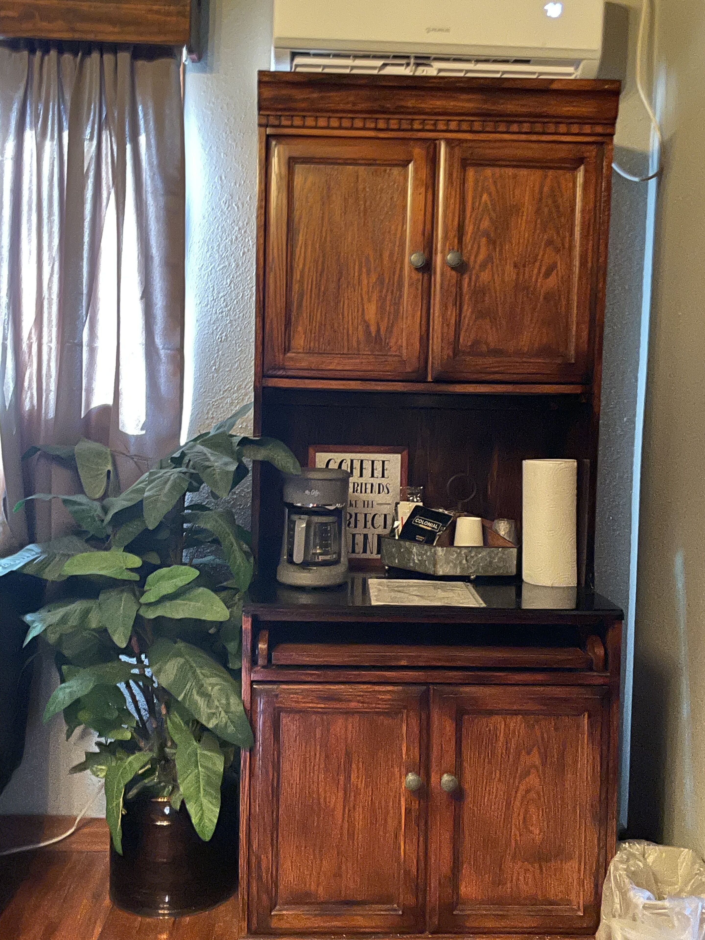 Un mueble de madera con una cafetera y una planta en maceta sobre una mesa.