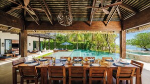 A dining area with a pool view, wooden furniture, and ceiling fans. - Perfect Family Retreat with the best Sunset views: Luxury Beachfront house w/ Pool & Heated Jacuzzi (Hacienda Pinilla)
