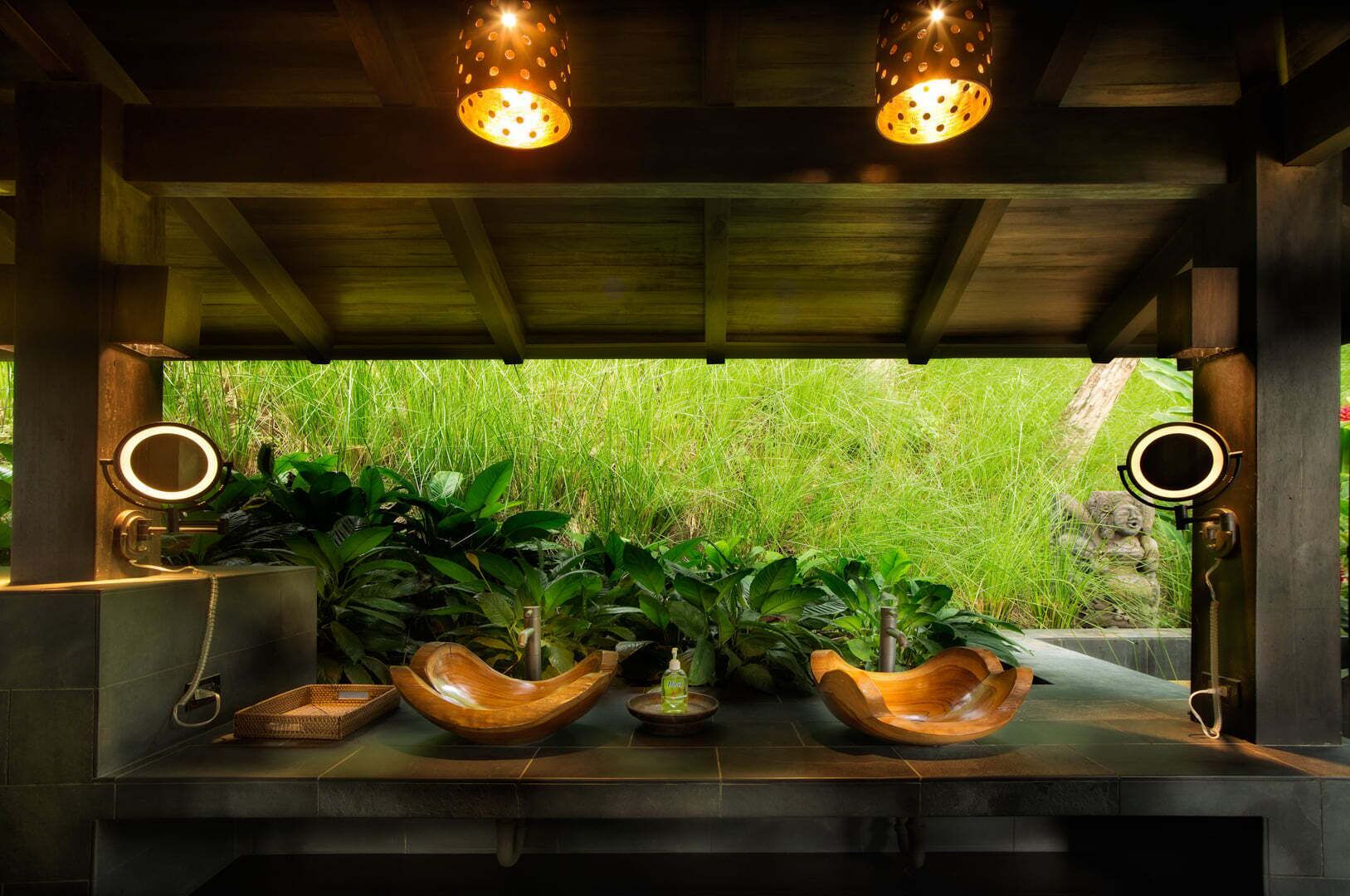 Un plafond en bois orné de deux suspensions, une fenêtre donnant sur une pelouse verdoyante, et une table en bois sur laquelle sont posés un miroir et un bol.