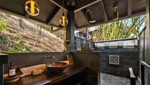 Une salle de bain moderne avec un grand lavabo, un plan de toilette en bois et une vue sur des bambous à l’extérieur.