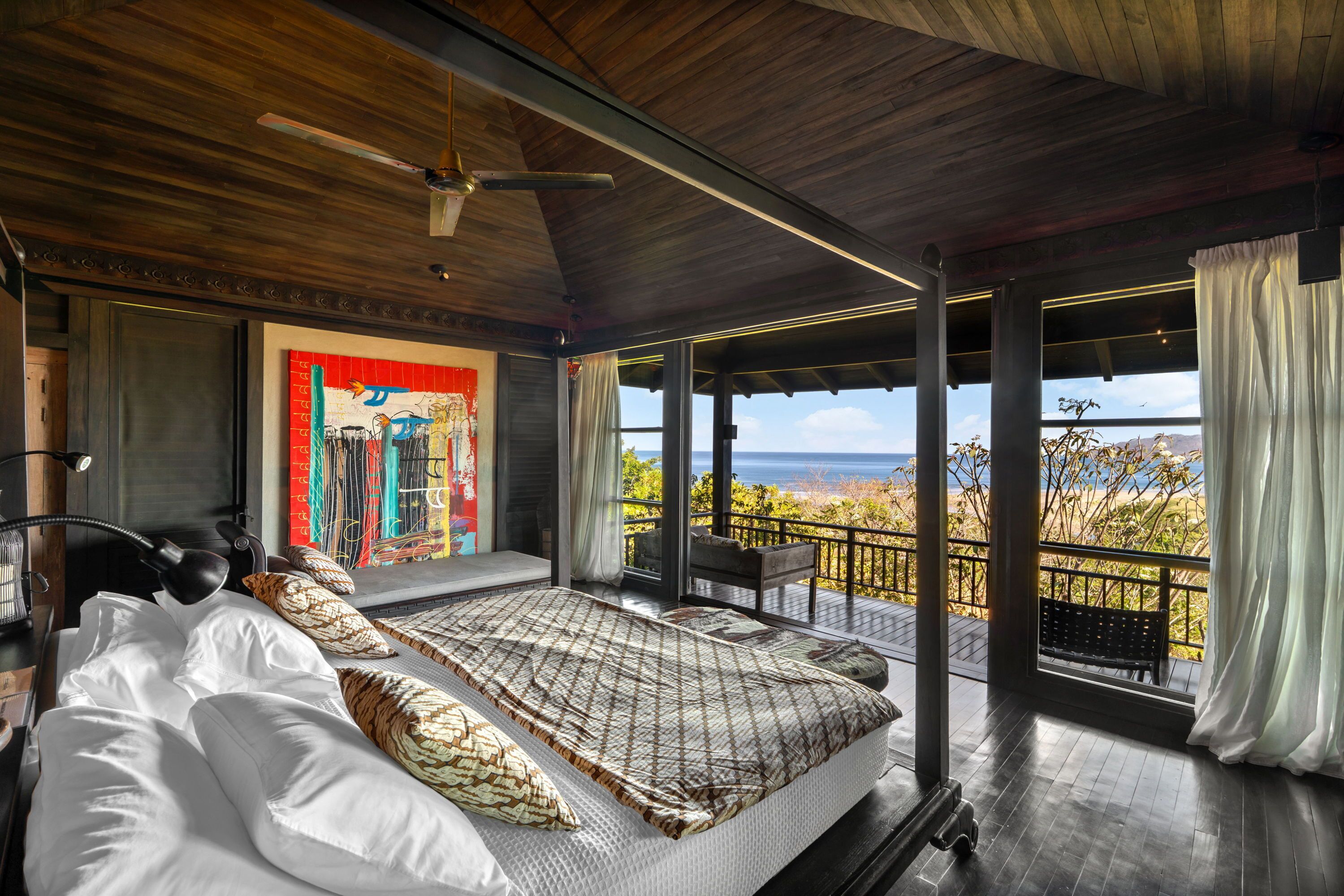Un dormitorio con una cama grande, un ventilador de techo y vista al océano.