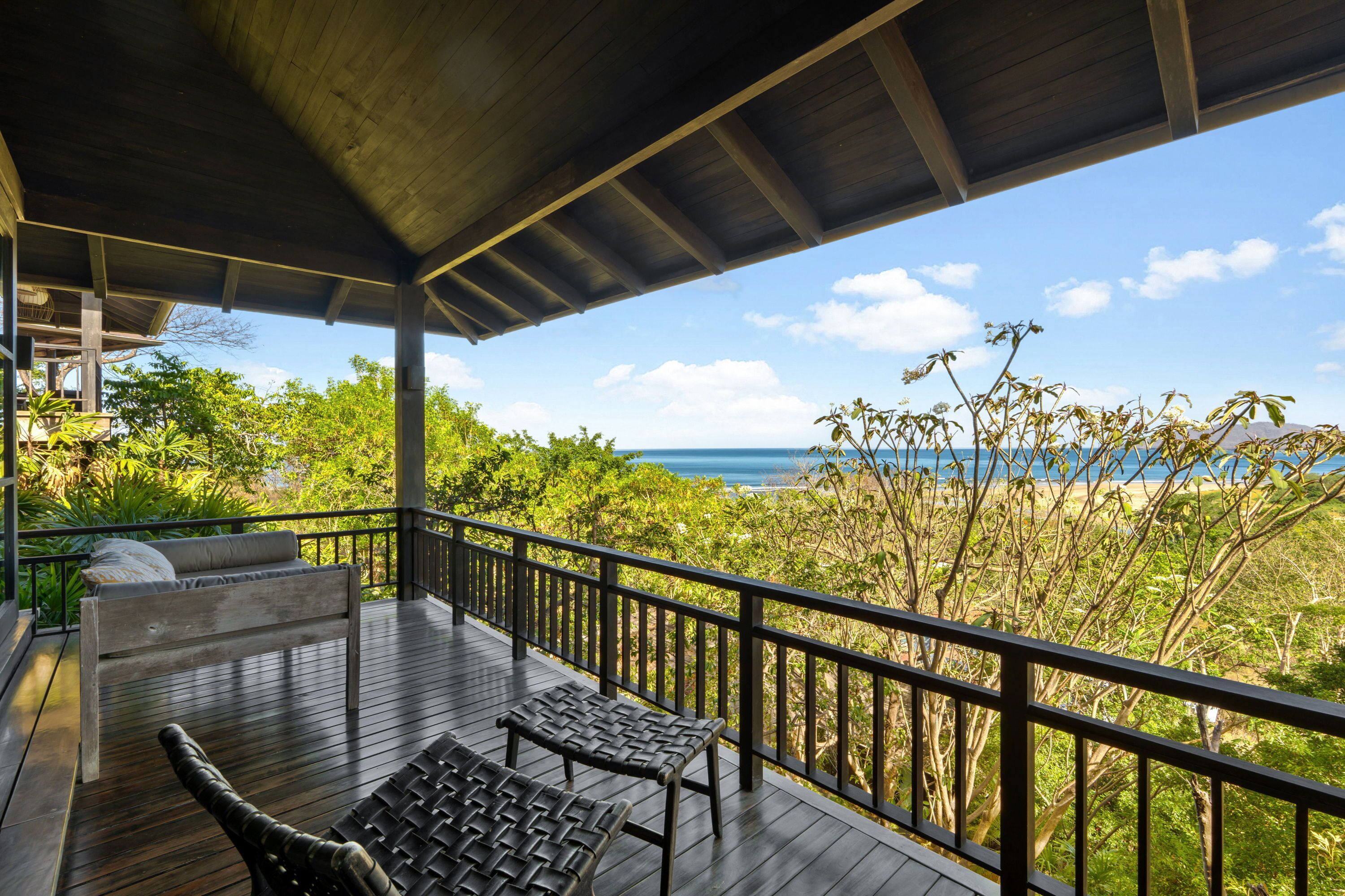 A wooden deck with a bench and a table, overlooking a lush landscape and the ocean.