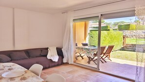 Une pièce comprenant un canapé, une table à manger et une porte-fenêtre coulissante donnant sur un espace extérieur équipé d’une table et de chaises.