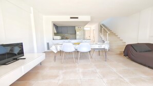 Un salon moderne comprenant un téléviseur, une table à manger avec des chaises, un canapé et un escalier menant à l’étage supérieur.