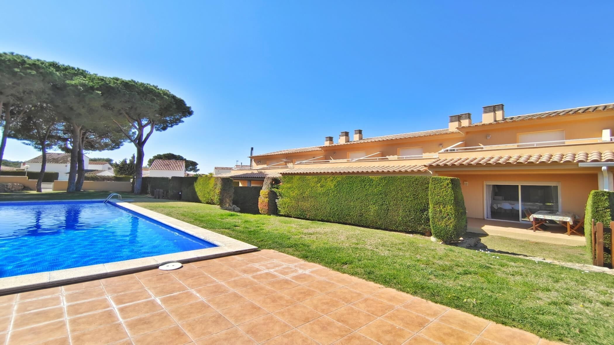 A residential property with a swimming pool, a well-maintained lawn, and a house with a tiled roof.