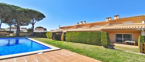 A residential property with a swimming pool, a well-maintained lawn, and a house with a tiled roof.