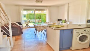 Une cuisine compacte équipée d’un lave-linge, un coin repas avec une table et des chaises, et un canapé dans le salon attenant.