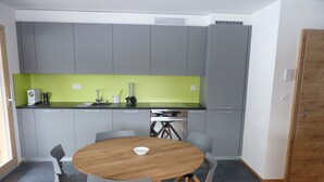 A compact kitchen with grey cabinets, a green backsplash, and a round wooden table with grey chairs. - Cosy apartment for 4 guests with WIFI, TV and balcony (Ovronnaz)