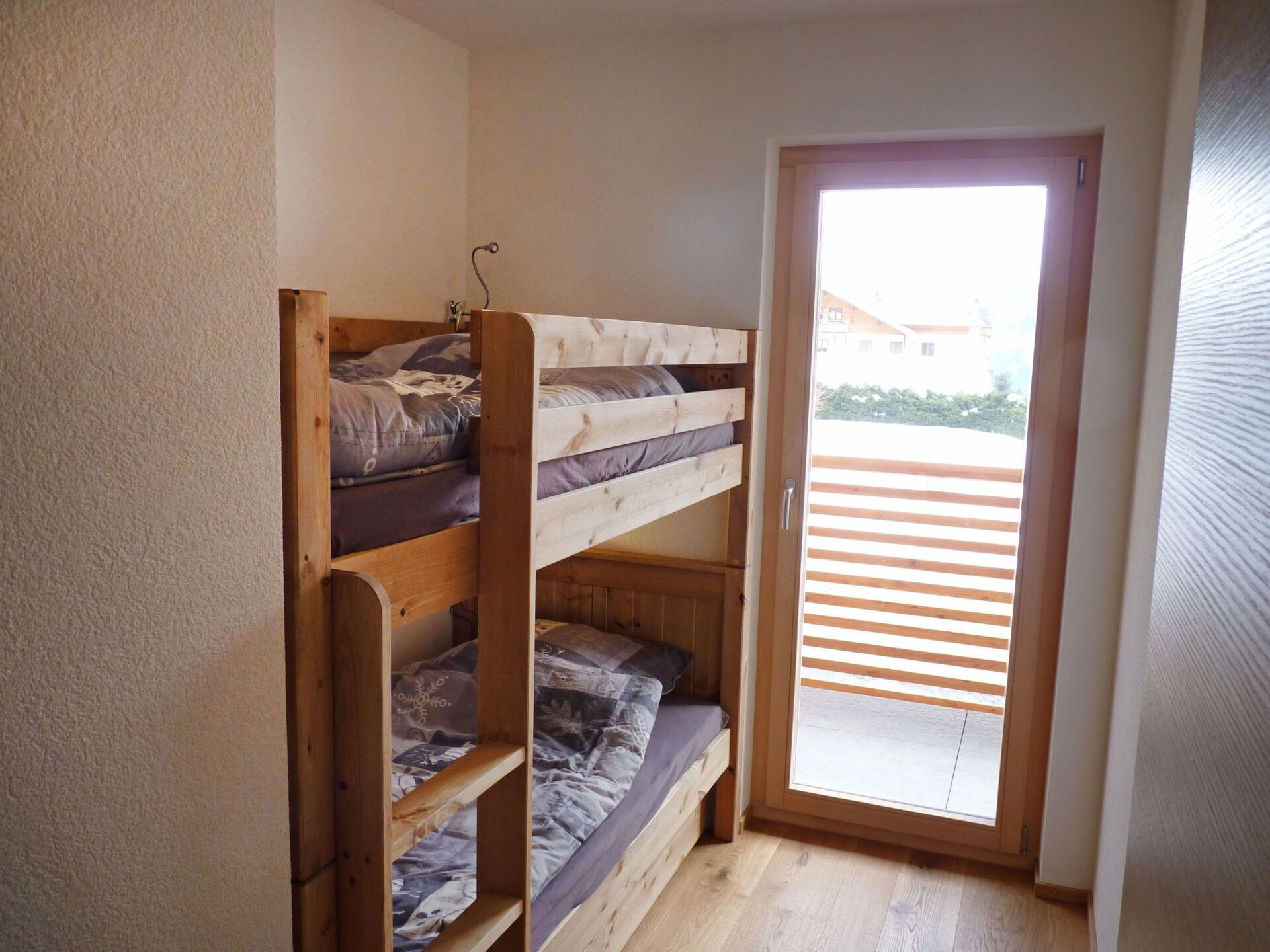 A small room with a wooden bunk bed and a sliding glass door leading to a balcony.