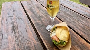 A picnic table with a glass of beer and a sandwich.