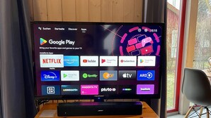 A television on a wooden stand with a bookshelf below it, displaying a Google Play interface with various app icons.