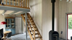 A room with a wooden staircase, a black wood stove, a dining area with a red lamp, and a cabinet with glass doors.