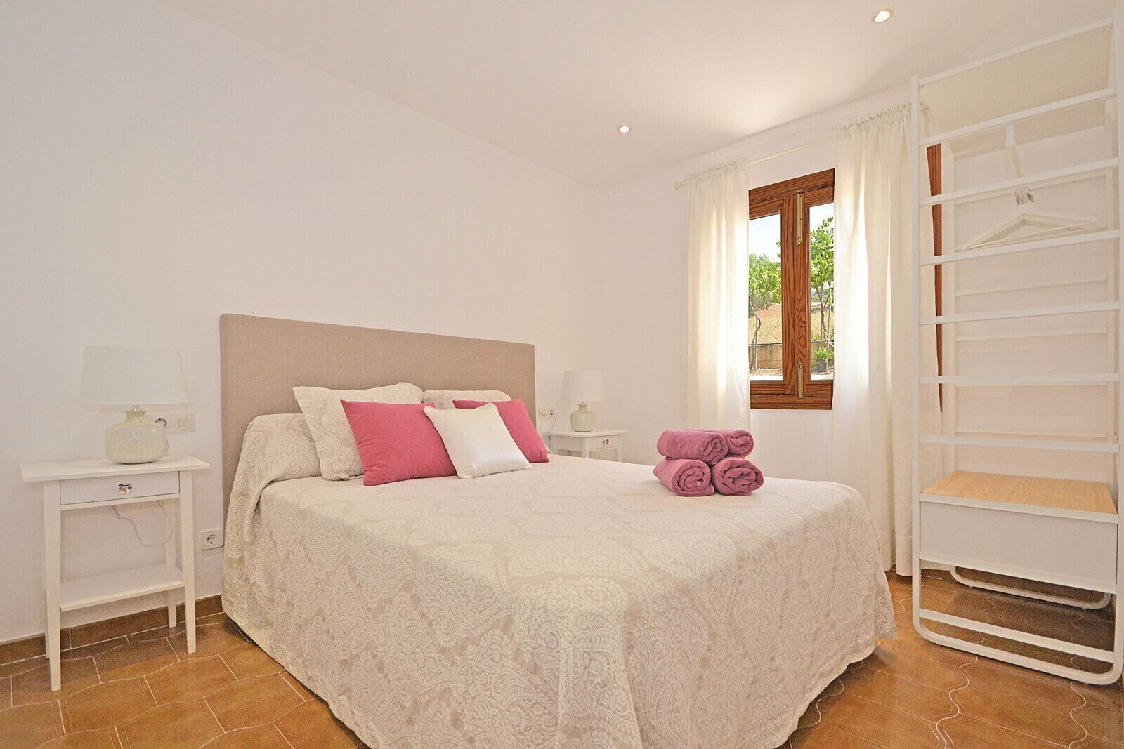 Une chambre à coucher bien aménagée, avec un lit, des tables de chevet, une fenêtre avec des rideaux et une armoire intégrée.