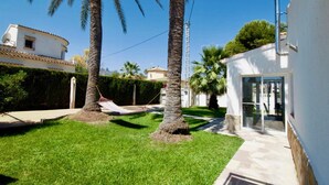 Un jardin bien entretenu, agrémenté de palmiers, d’un hamac et d’un bâtiment blanc doté d’une porte en verre.
