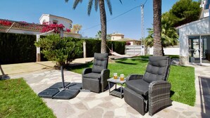 Une terrasse extérieure avec deux fauteuils gris rembourrés et une petite table sur laquelle sont posés deux chopes de bière.