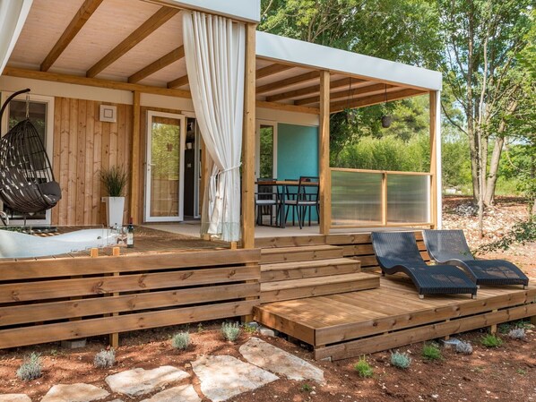 Une terrasse en bois avec des chaises longues, un fauteuil suspendu et un espace patio couvert comprenant une table et des chaises.