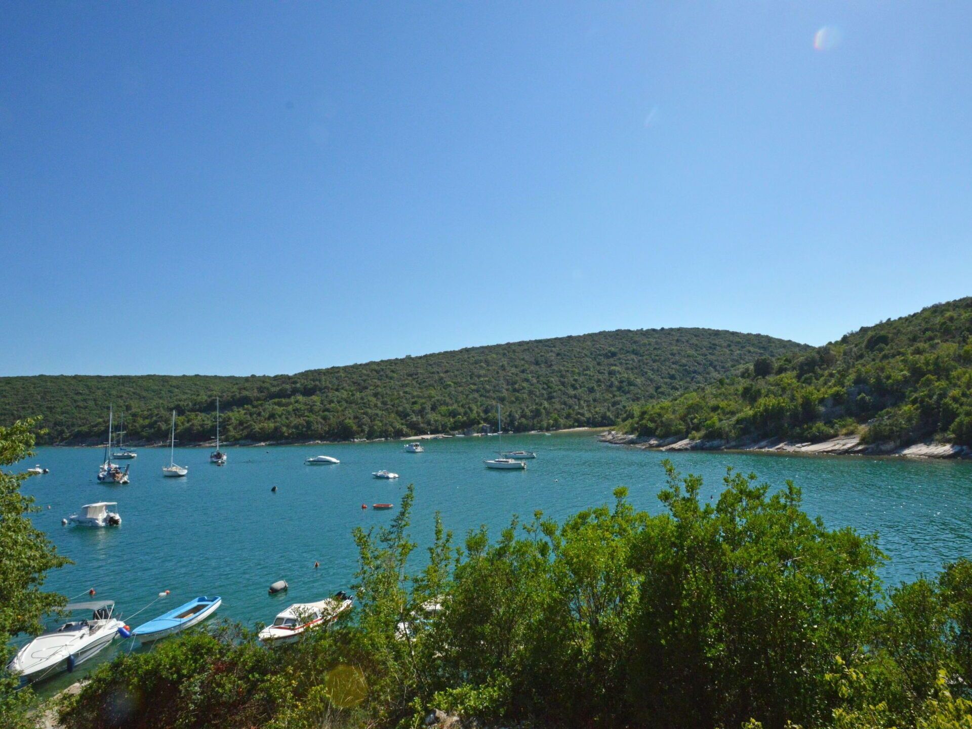 A coastal bay with several boats anchored near the shore, surrounded by lush green hills.