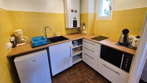 Una cocina compacta con un lavamanos, una cafetera, un hervidor y un refrigerador pequeño.