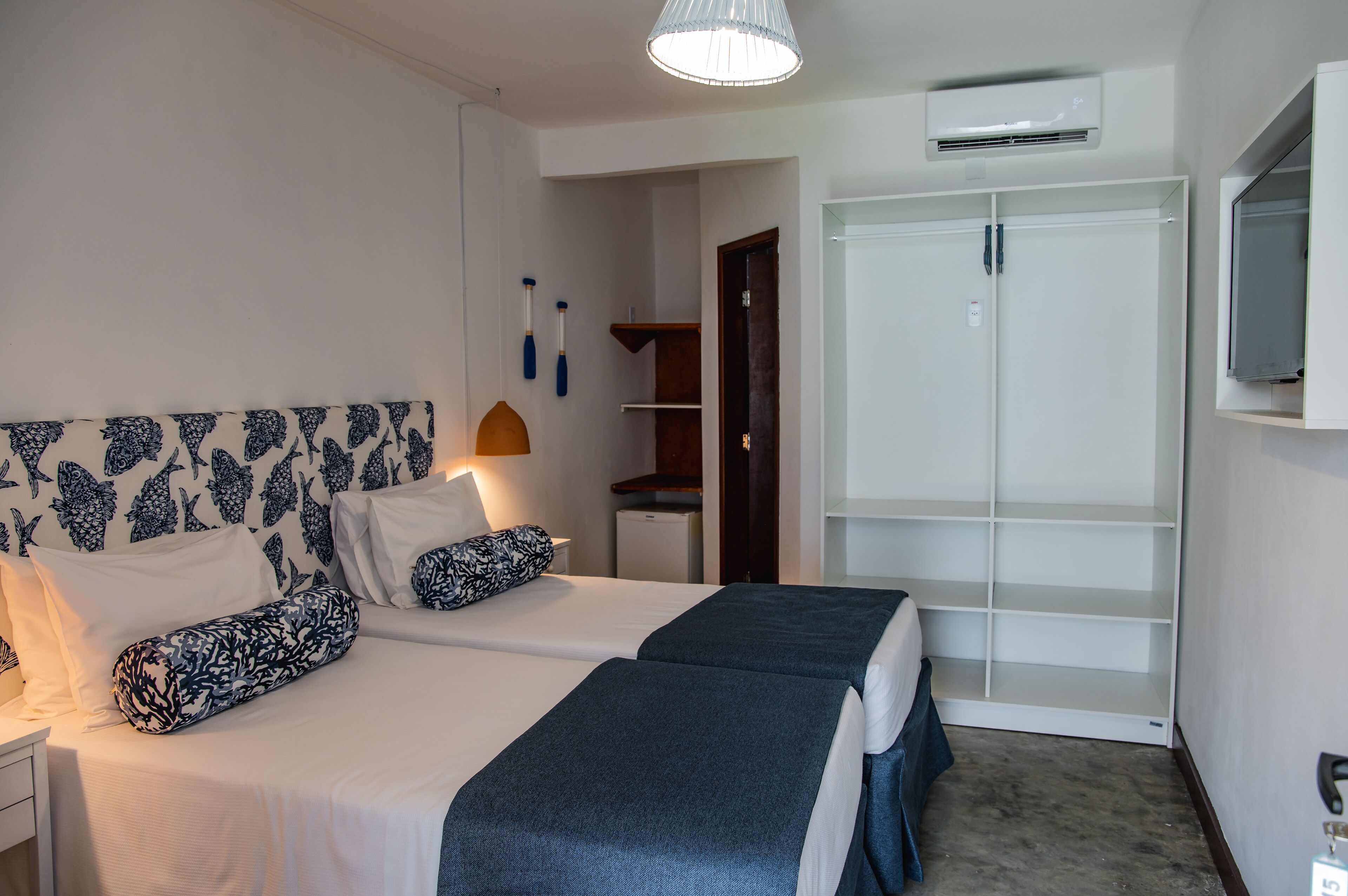 A hotel room with two beds, a wardrobe, a TV, and an air conditioning unit.