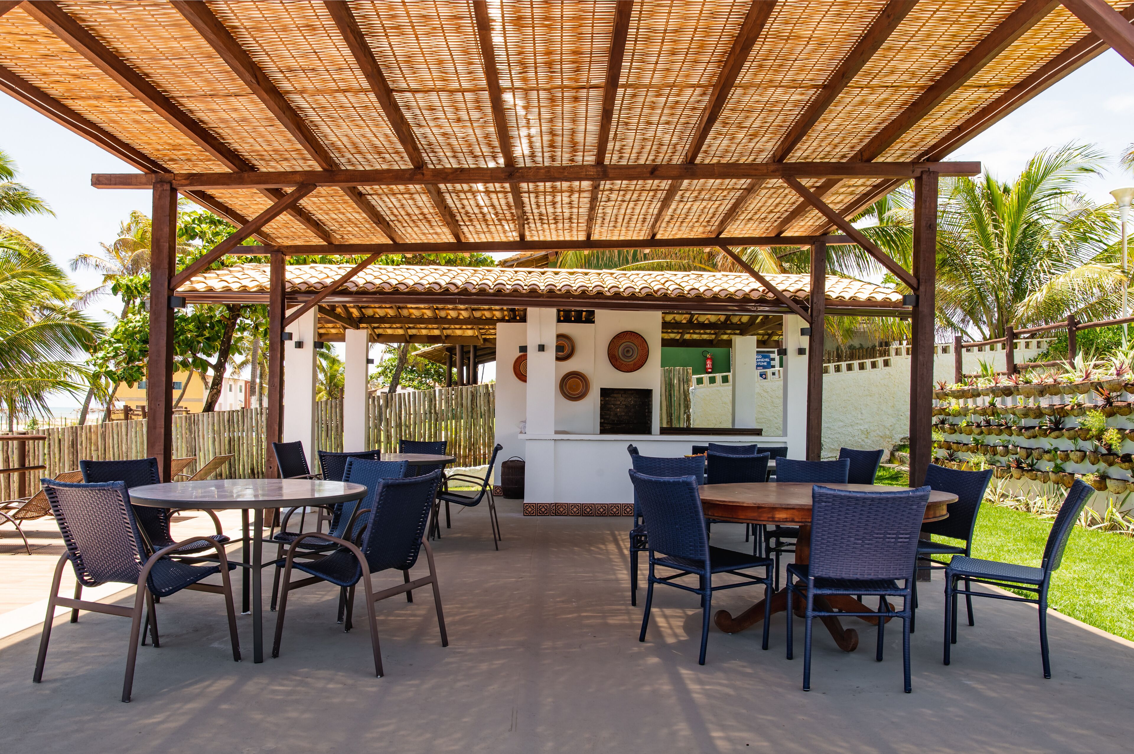 Een terras buiten met tafels en stoelen, een overdekt gedeelte met een betegeld dak en uitzicht op de oceaan.