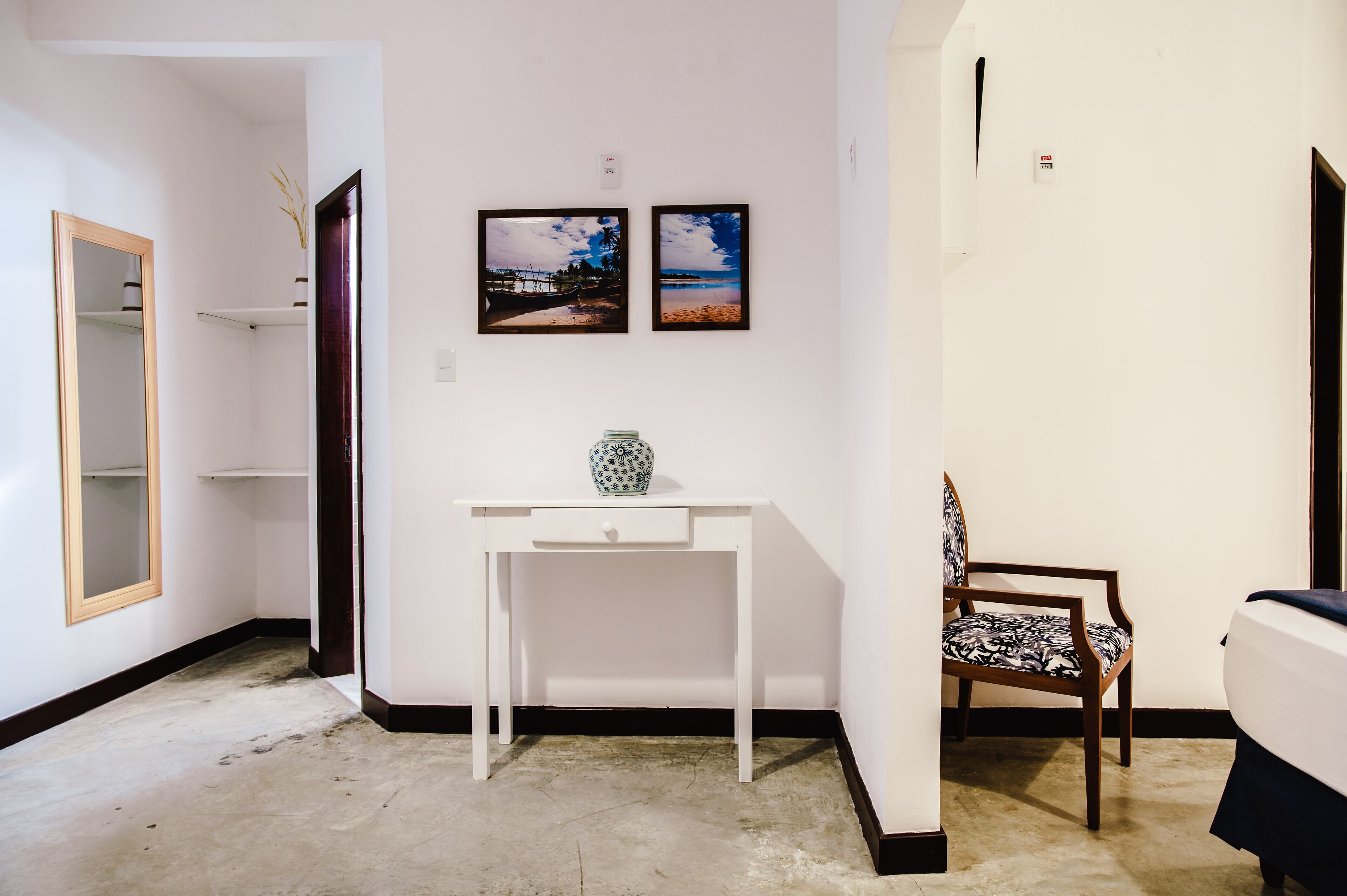 A room with a white desk, a chair, a bed, and two framed pictures on the wall.