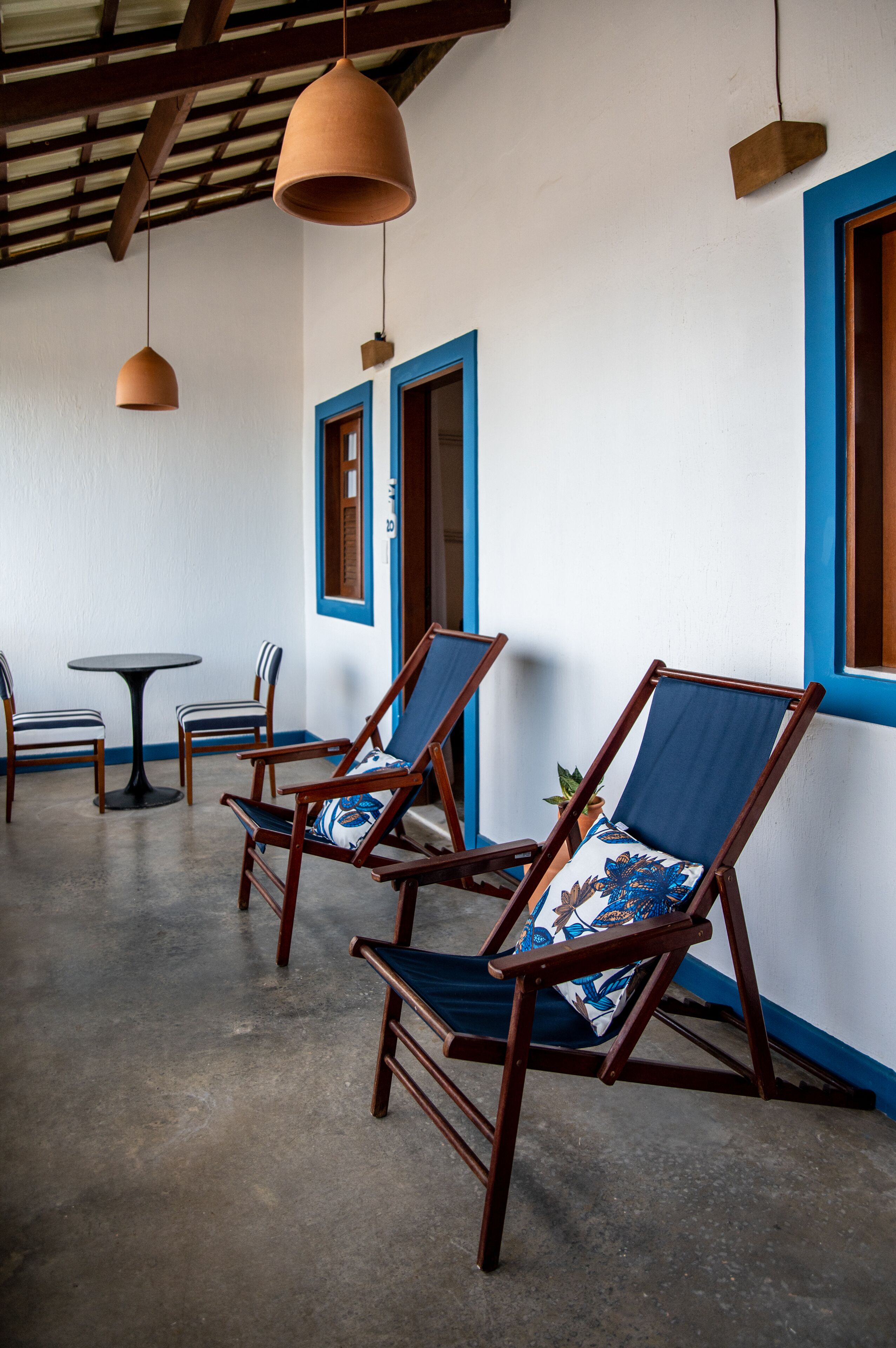 Una habitación con dos sillas de madera con cojines azules, una mesita redonda pequeña y lámparas colgantes de terracota.
