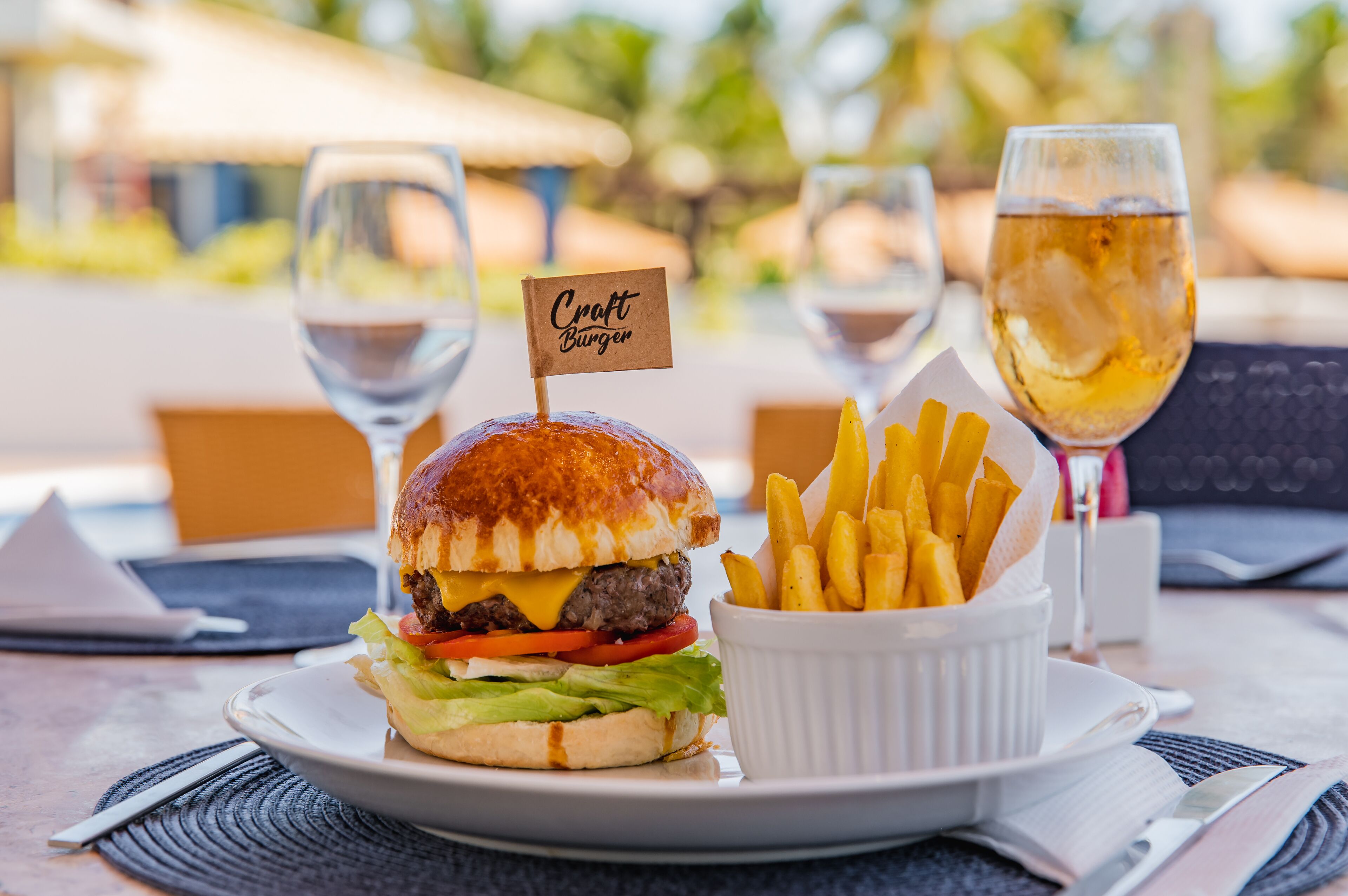A meal consisting of a burger, fries, and a glass of beer on a table with a placemat and napkin.