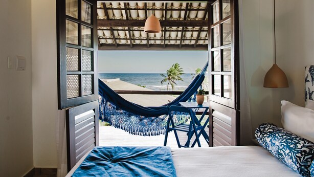 Un dormitorio con vista a la playa, una hamaca y una cama con cubrecama azul.