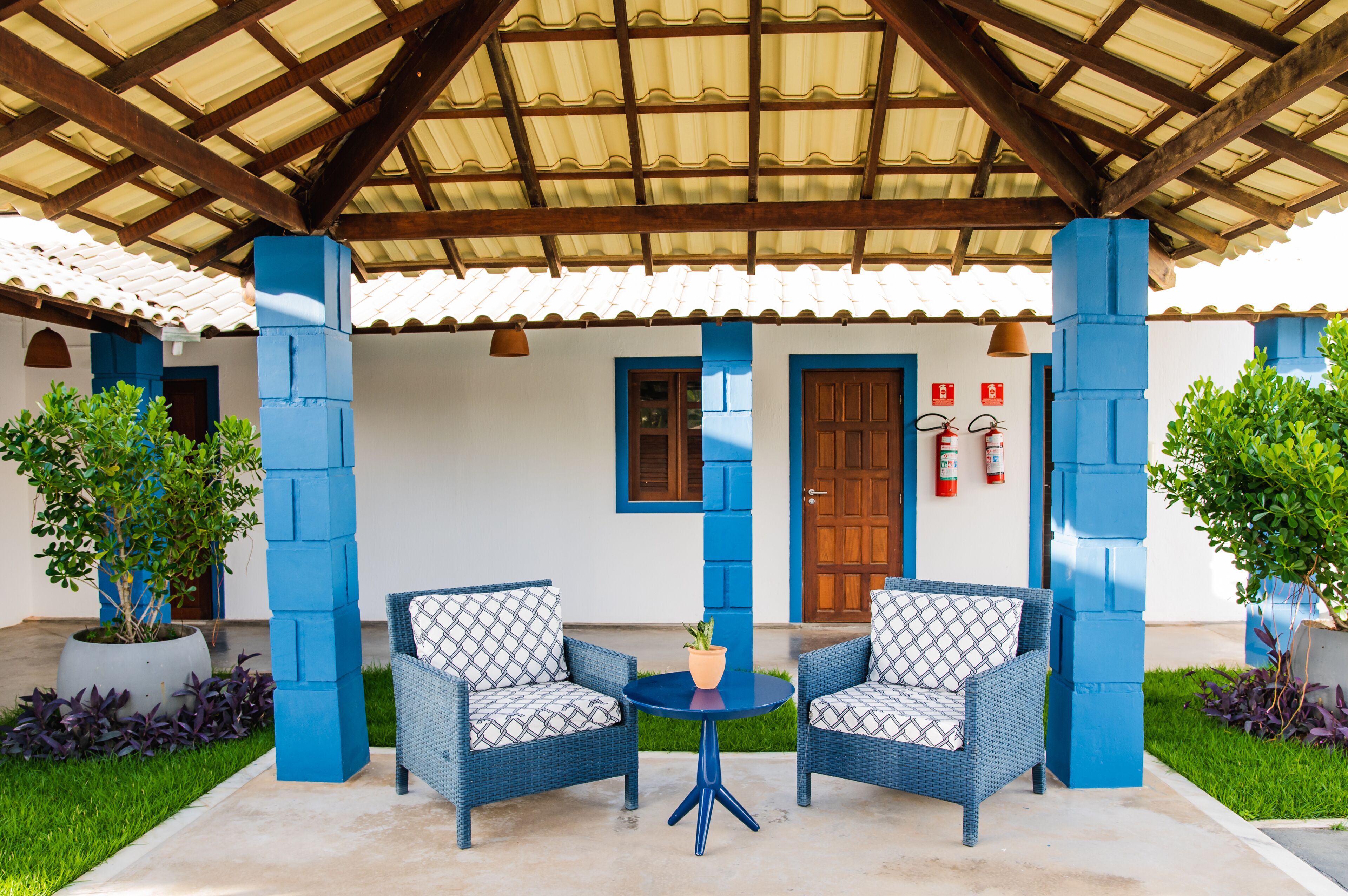 A covered patio area with two wicker chairs, a small round table, and potted plants.
