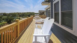 Una terraza de madera con sillas y una mesa blancas, con vistas a un paisaje verde.