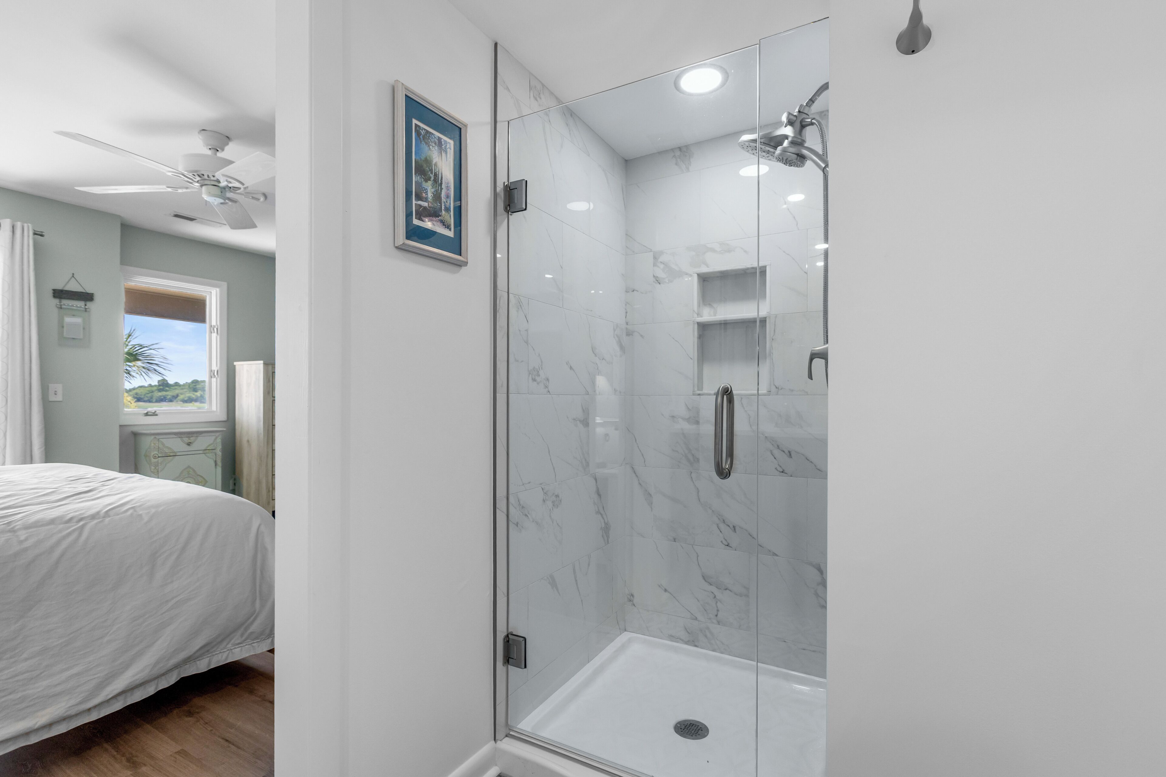 Un dormitorio con cama, ducha de vidrio y pared de mármol, y ventilador de techo.