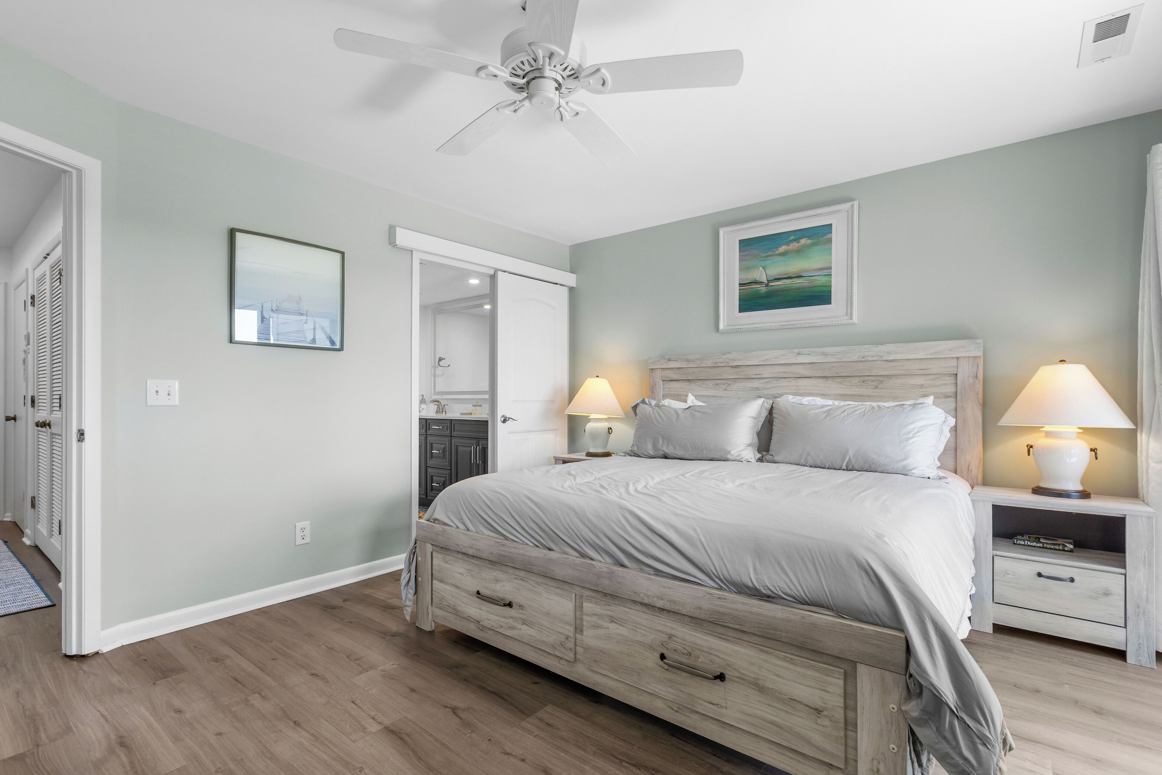 A bedroom with a bed, bedside tables, a ceiling fan, and a door leading to a bathroom.