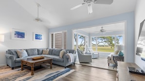 A spacious living room with a gray sofa, a wooden coffee table, and a view through large windows to the outdoors.