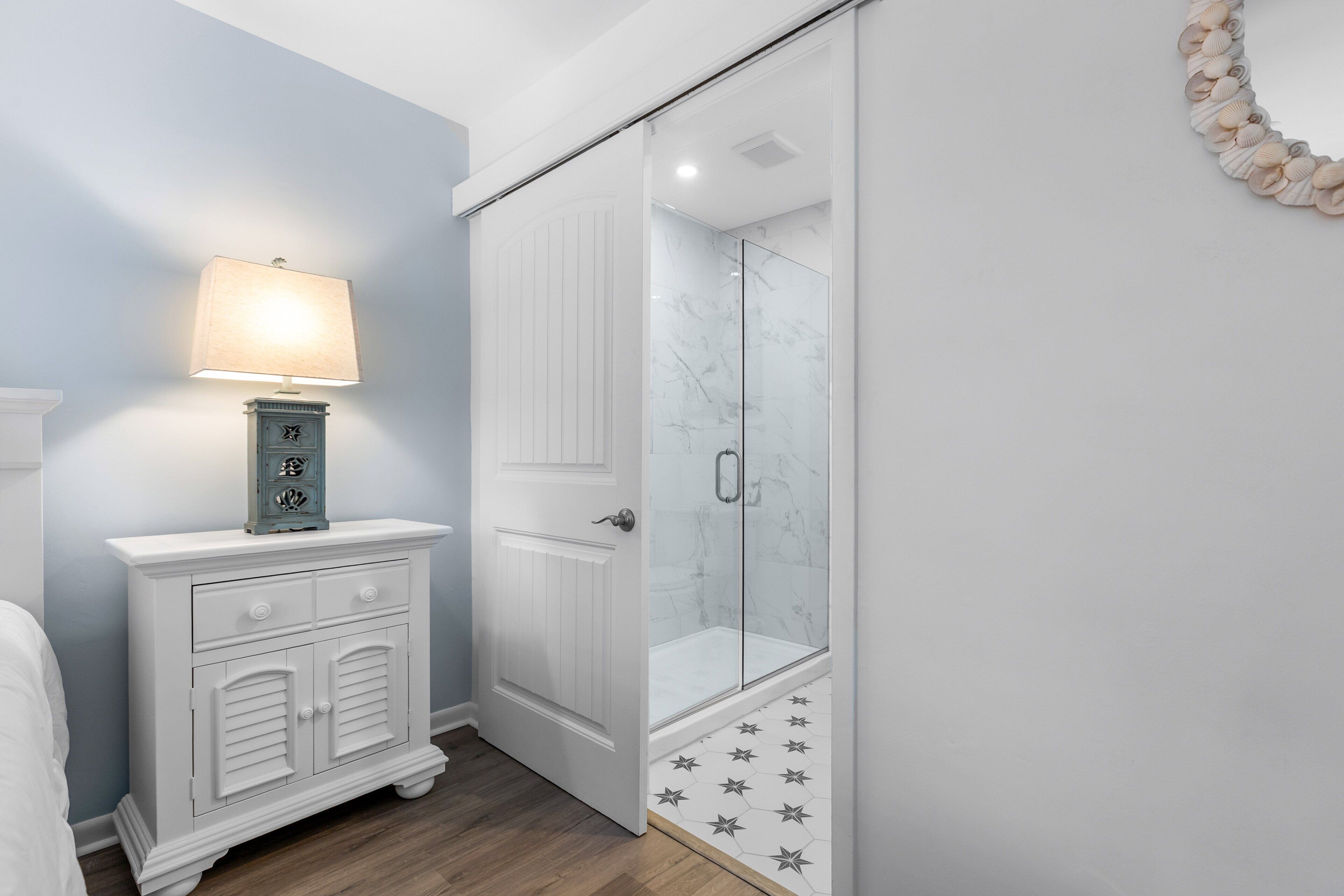 A bathroom with a shower, a vanity with drawers, a wall-mounted lamp, and a decorative wall piece.