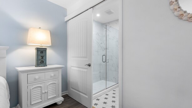 Une salle de bain avec une douche, un meuble-lavabo avec des tiroirs, une lampe fixée au mur et un élément décoratif mural.