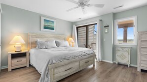 A bedroom with a bed, nightstands, a ceiling fan, a window with a view, and a cabinet.