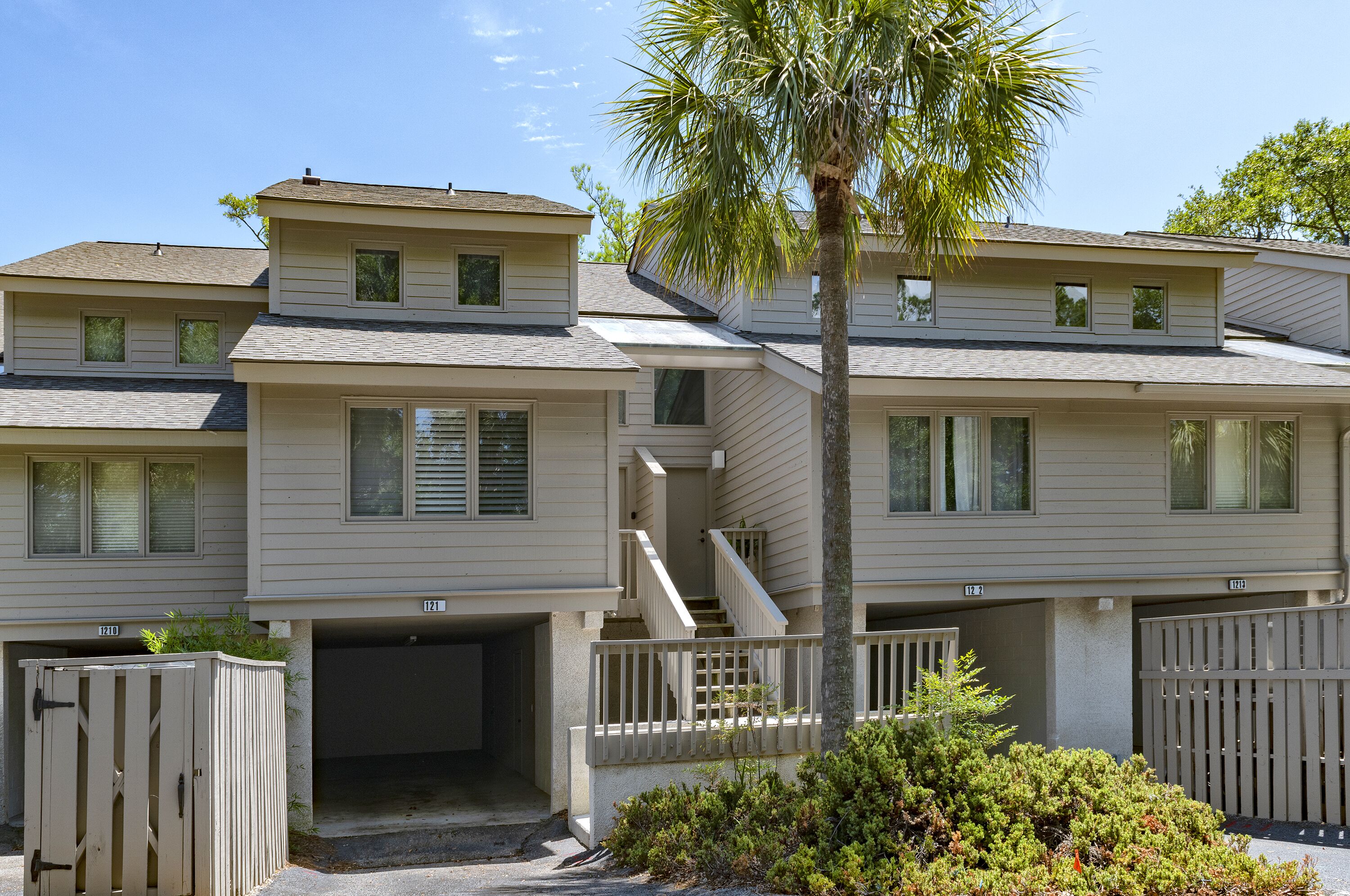 A multi-story residential building with a central staircase, a covered parking area, and a small garden with a palm tree.