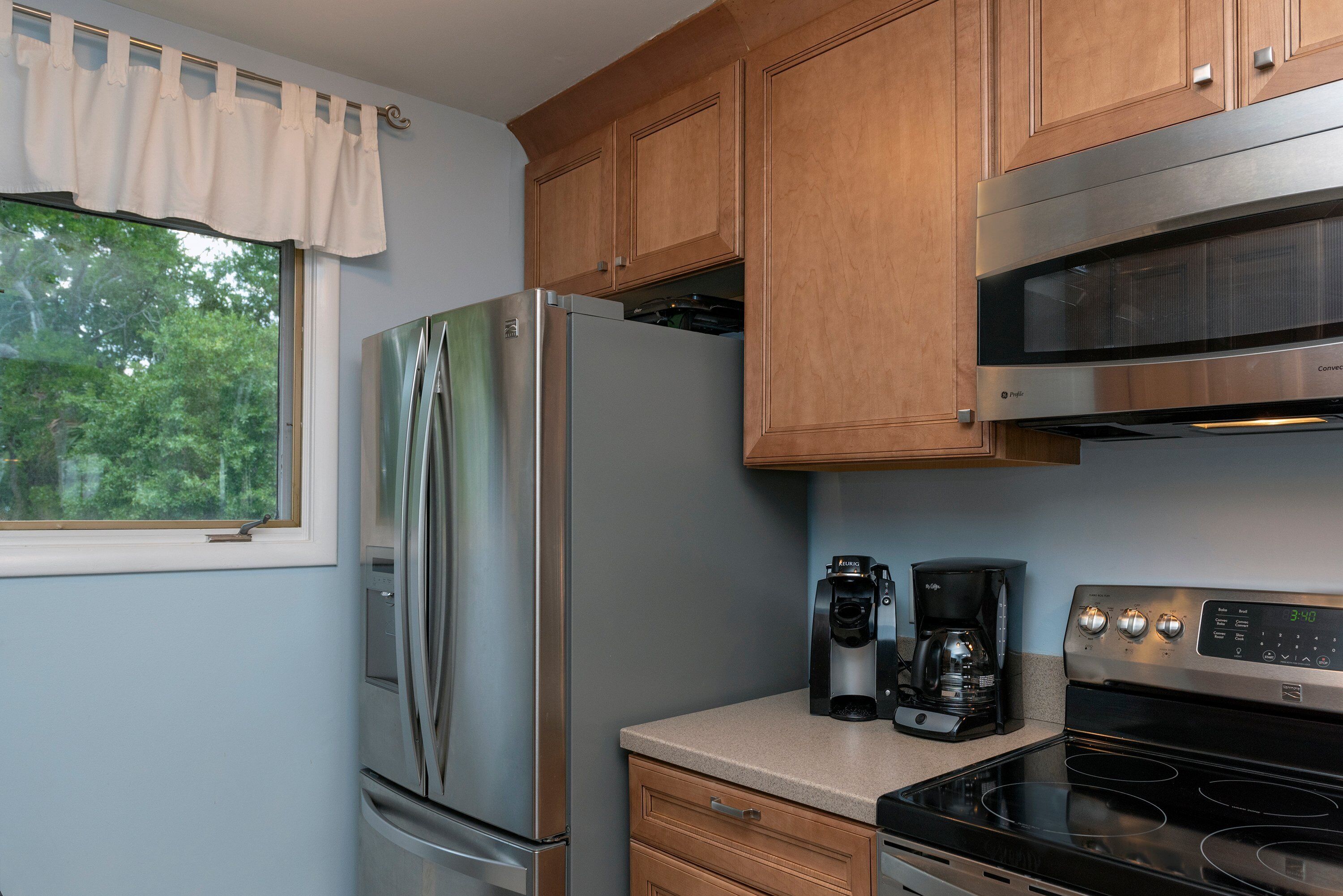 Una cocina compacta con armarios de madera, un refrigerador de acero inoxidable, una cafetera y una estufa.