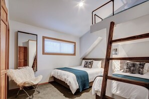 A bedroom with bunk beds, a chair, a window with blinds, and a mirror on the wall.