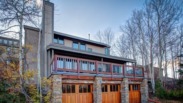 A modern two-story house with a stone facade, large wooden garage doors, and a balcony with a railing. - The Crescent Ridge, 2BR Ski Condo, Walk to Lifts! (Park City)