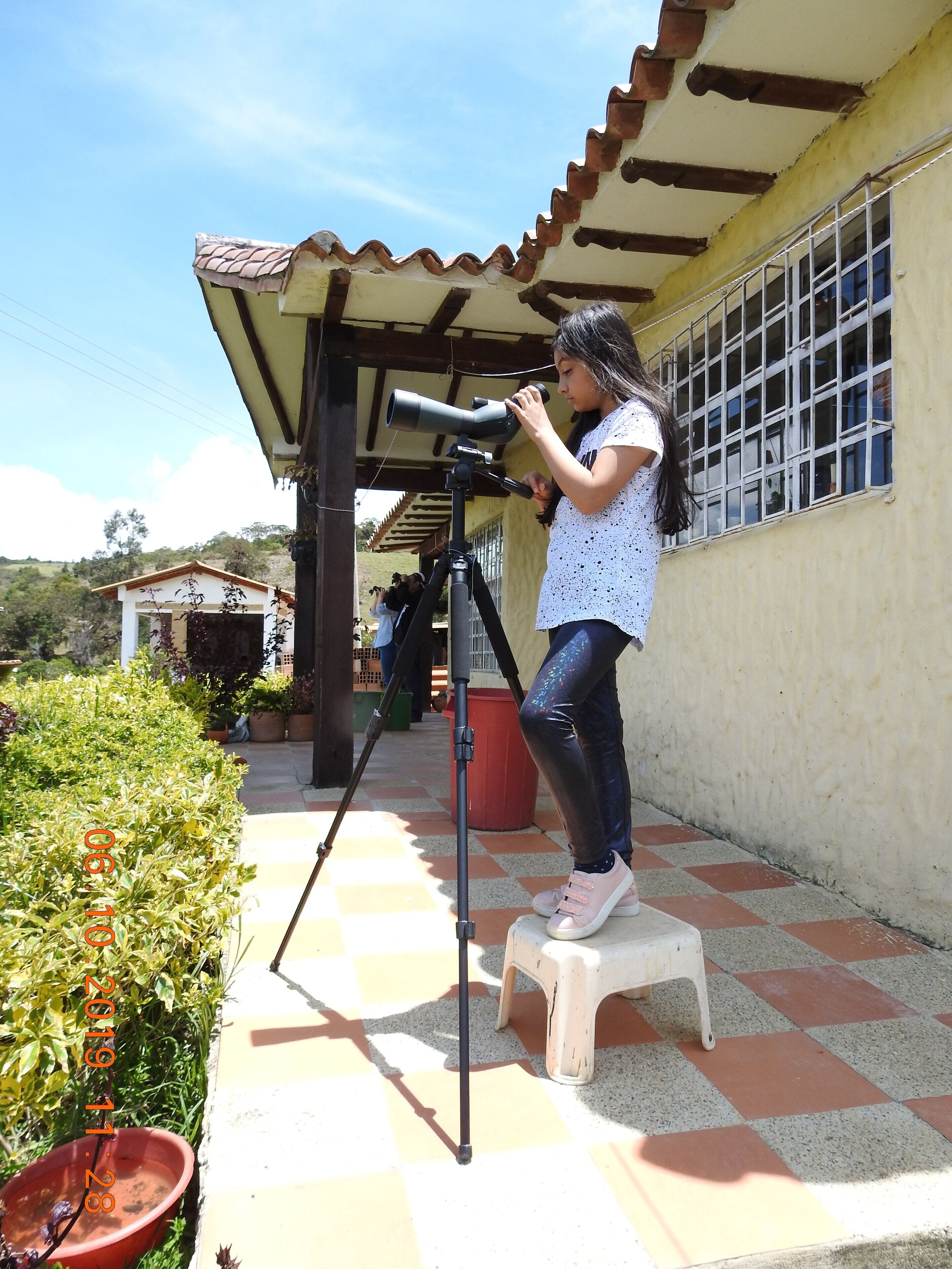 A person standing on a stool, adjusting a telescope on a tripod.