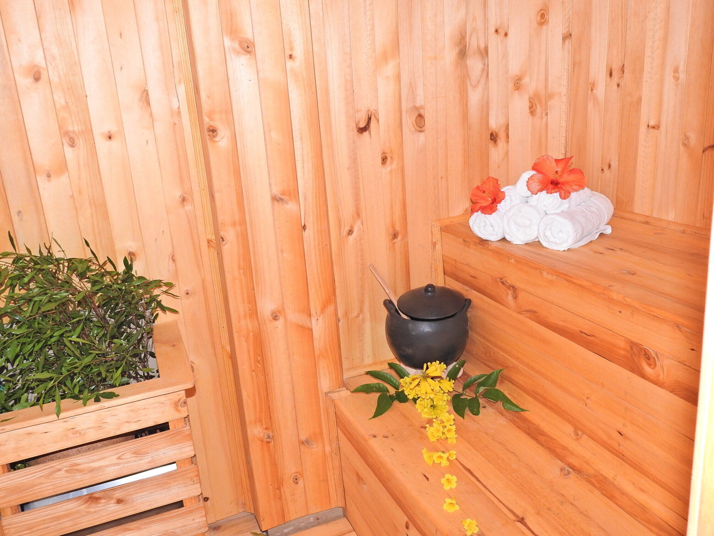 A wooden sauna with a black pot, towels, and a potted plant.